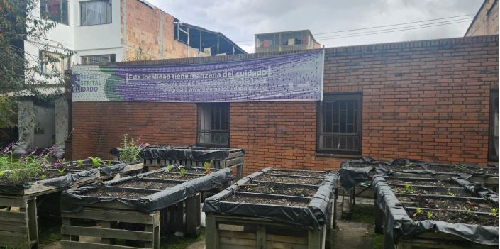 Women learn to plant and harvest a variety of fruits and vegetables. The banner reads, "This neighbourhood has a Block of Care" 