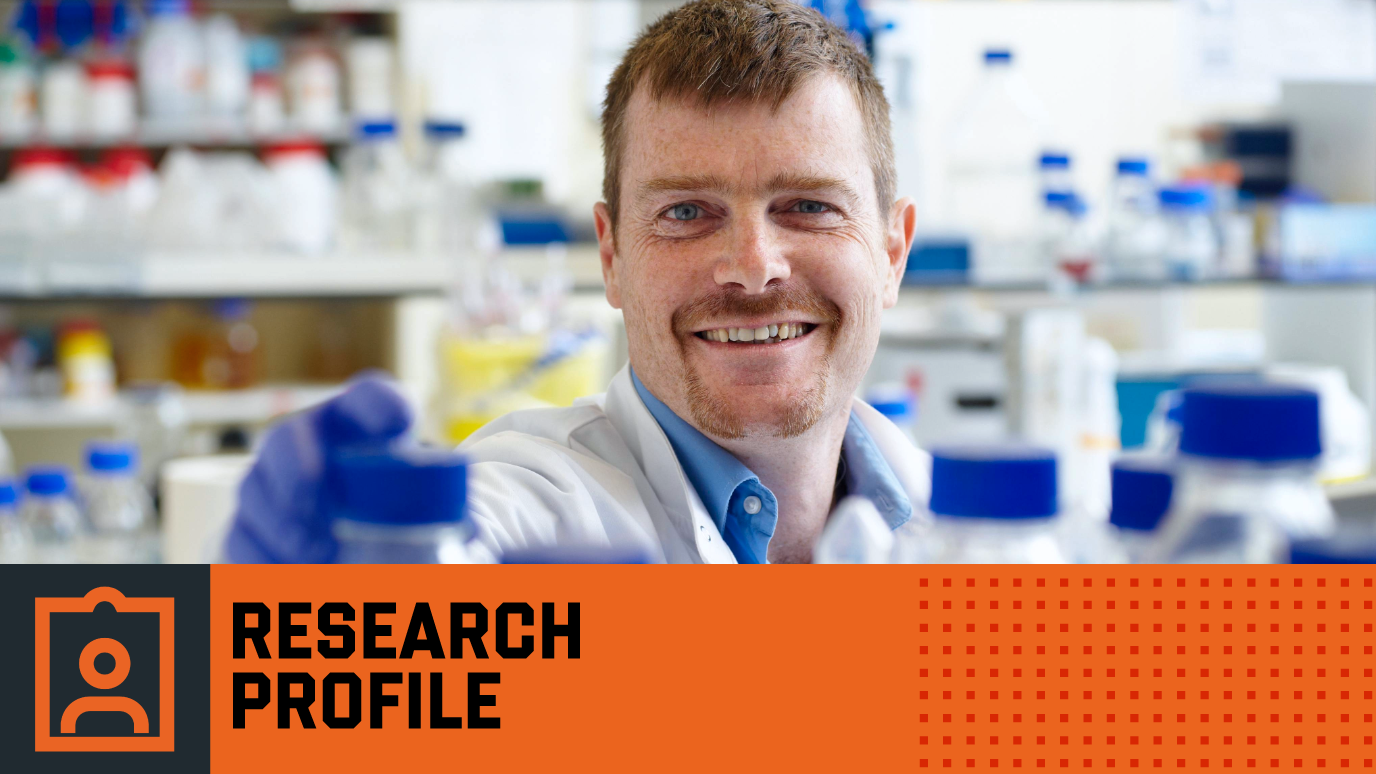 Photograph of Professor Robin Williams reaching for bottle in lab - Orange Research Profile banner with icon 